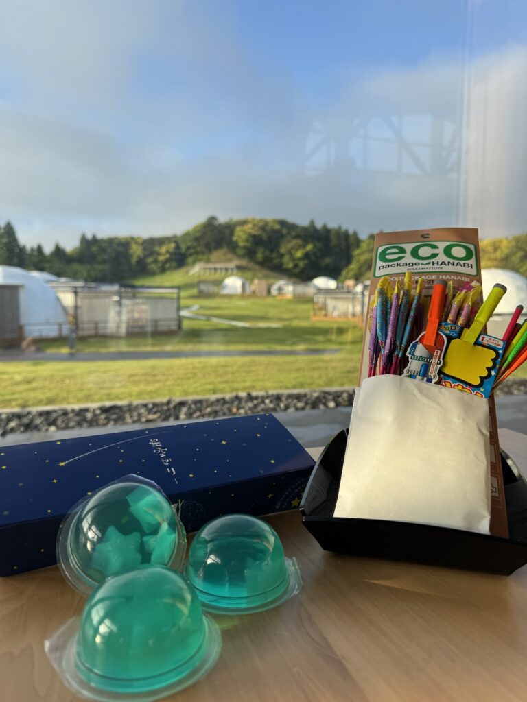 Close-up of teal plastic bubble domes and a colorful 'eco Hanabi' display box on a table, with an outdoor field in the background.