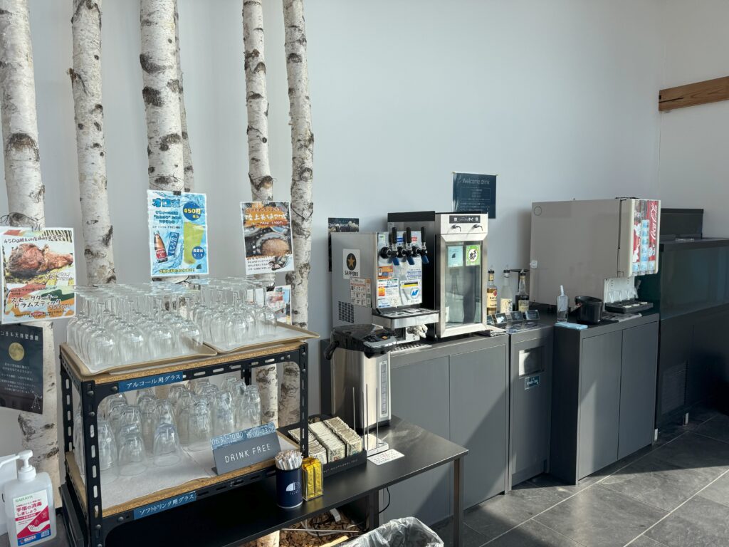 Cafe counter with birch tree trunks as wall decor, glassware on racks, and beverage dispensers in the background.